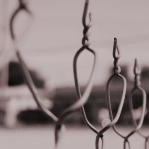 Close-up of a twisted wire fence with a blurred urban background, symbolizing social barriers and marginalization.