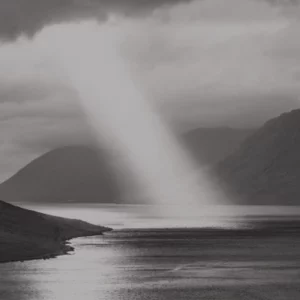 Beam of light breaking through clouds over a calm fjord landscape