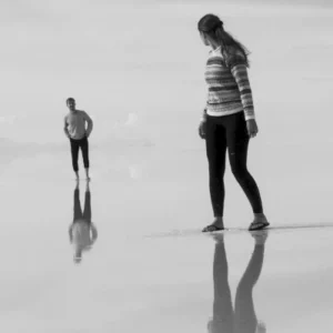 Black-and-white image of two people standing and walking on a reflective surface, symbolizing interaction, perception, and the construction of social reality in symbolic interactionism.